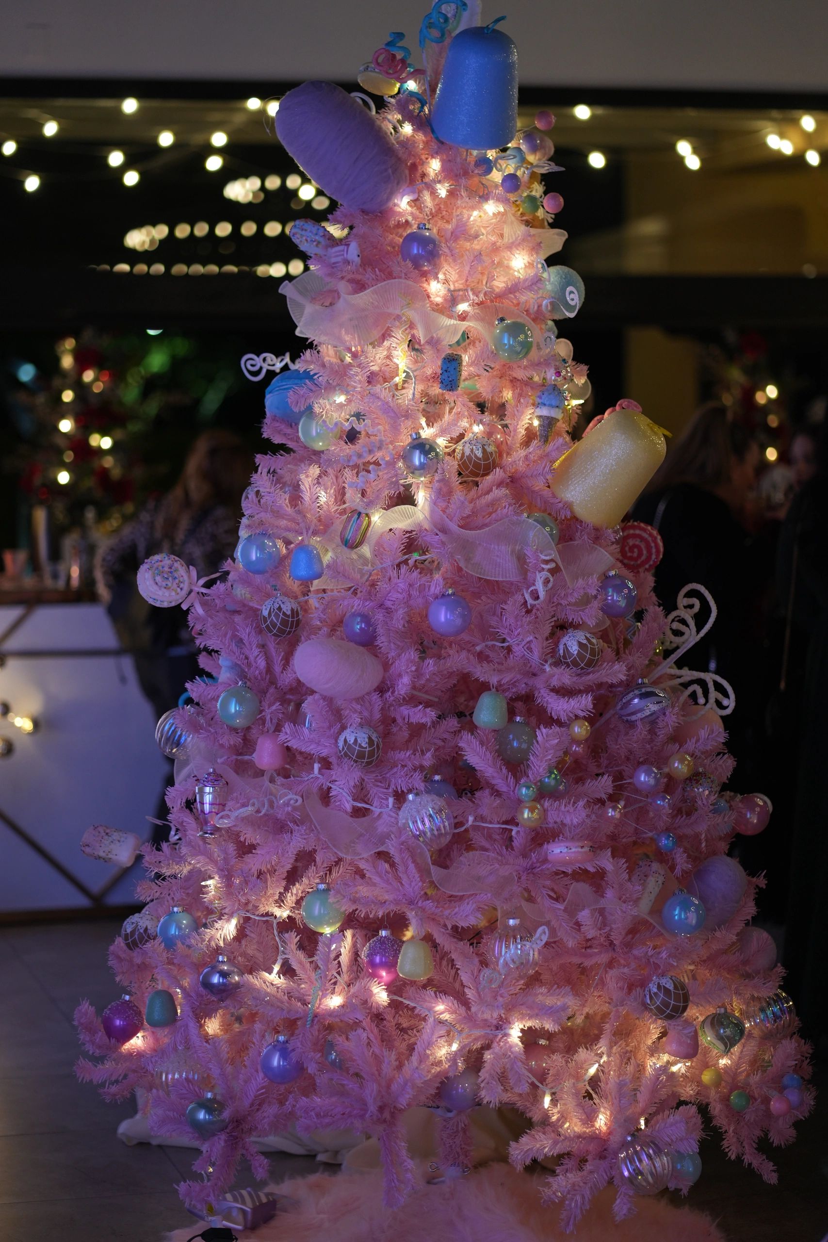 A pastel pink Christmas tree decorated with candy ornaments and ribbons